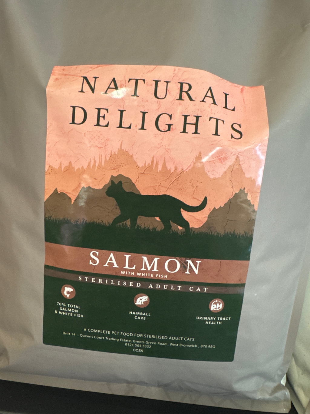 A bag of Natural Delights Salmon with Whitefish sterilised adult cat food, featuring a salmon-colored label with a black cat silhouette and green details on a light gray bag.